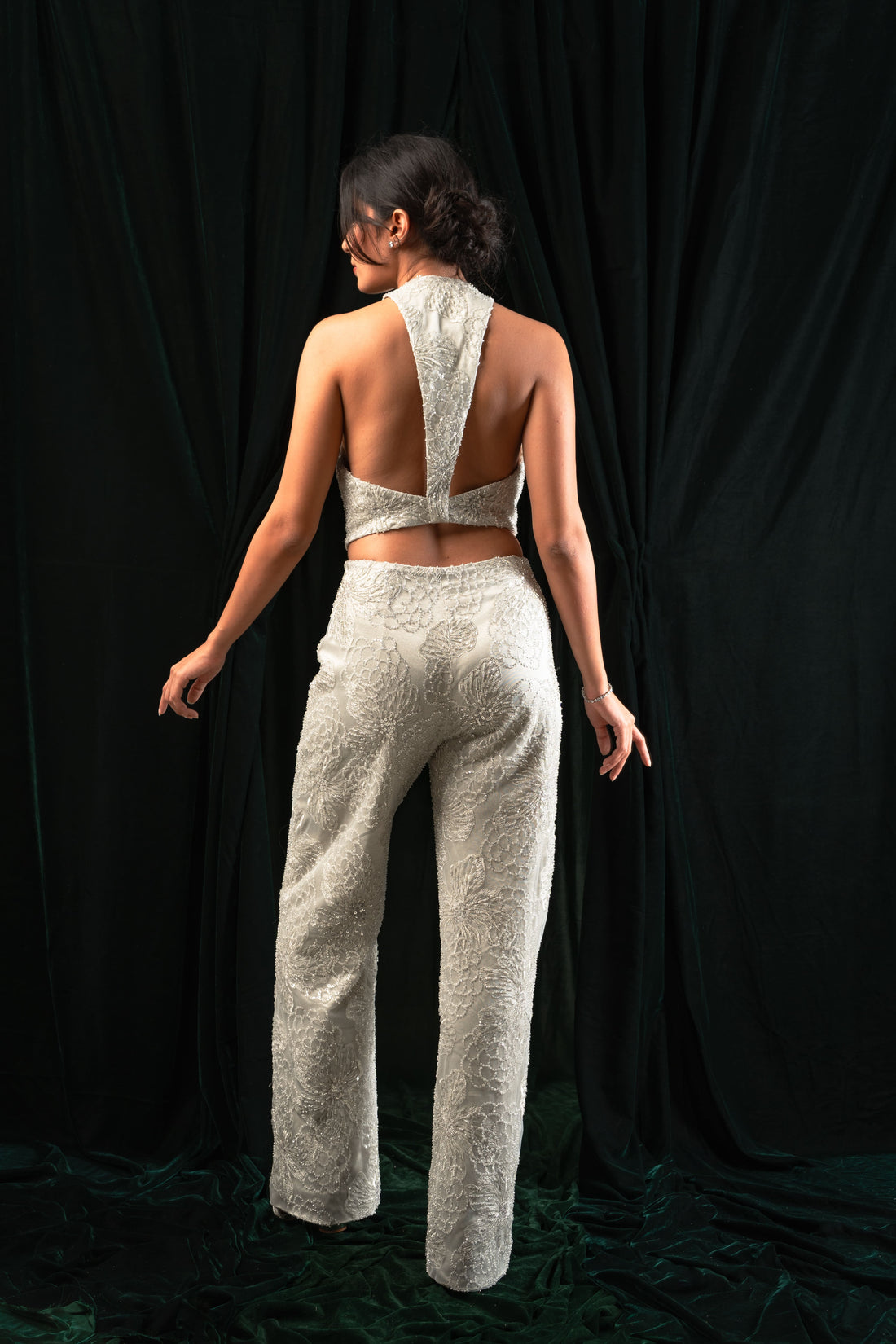 A model wearing straight-leg pants with embroidered details and a matching top, standing against a black background.